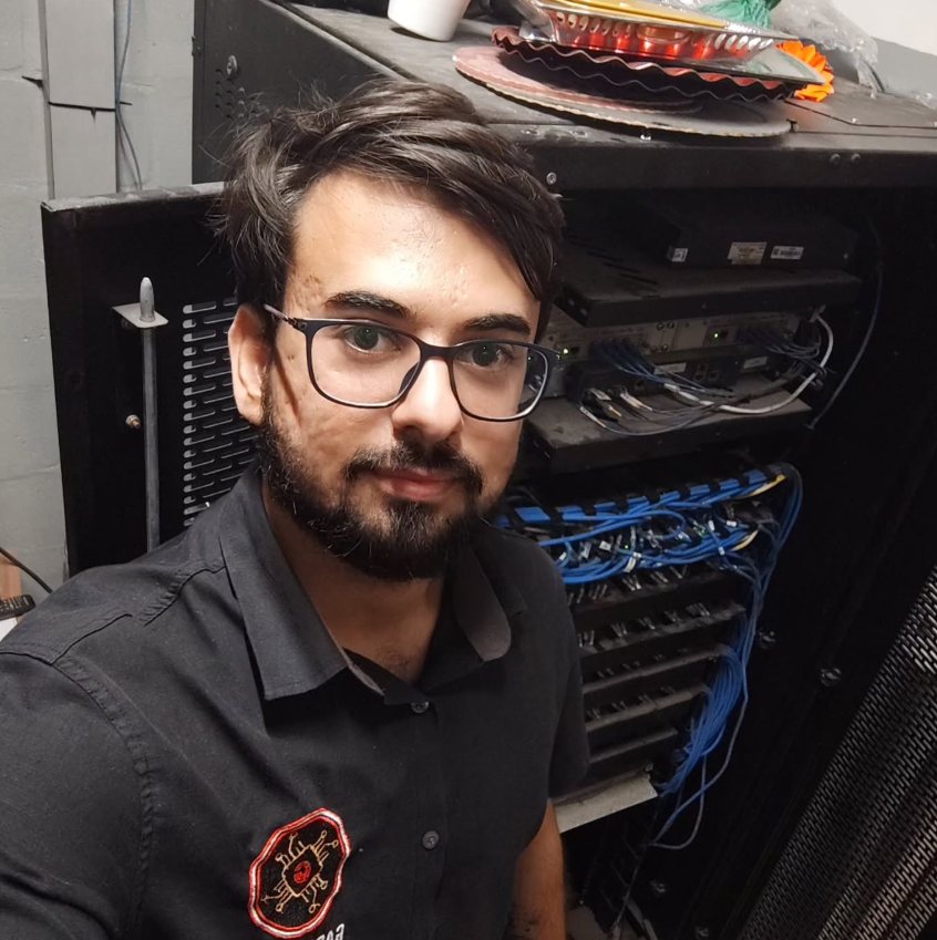 Antônio Garnica, de óculos e camisa preta com o logo da Garnica TI, em frente a um rack de rede
