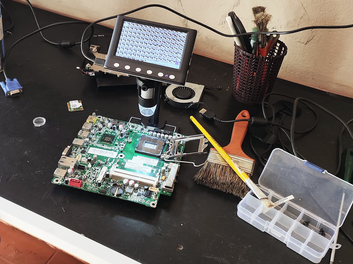 Bancada de reparo com uma placa-mãe aberta, microscópio digital e ferramentas