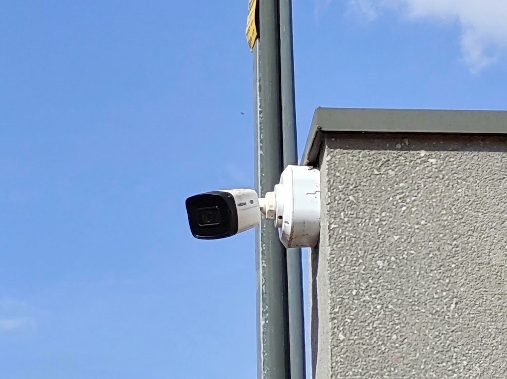 Câmera de segurança tipo bullet instalada em suporte na parede, contra o céu azul