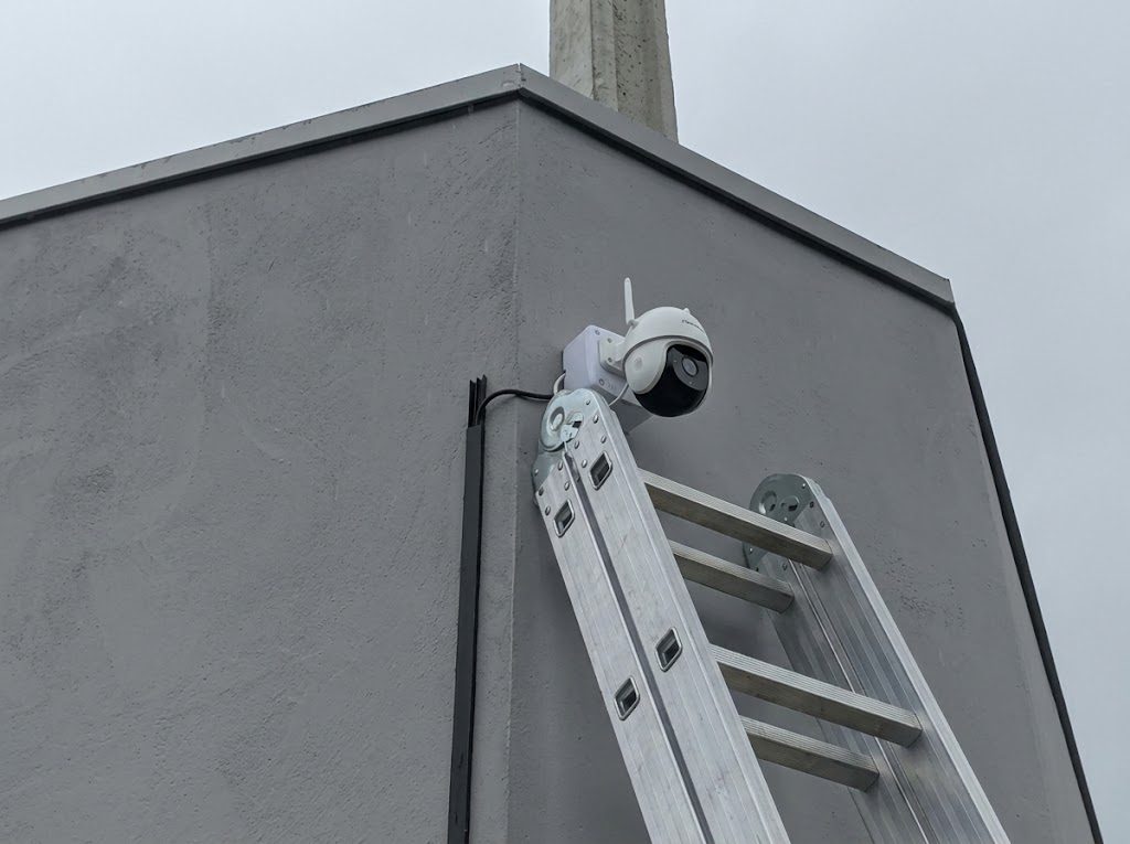 Câmera de segurança instalada no canto de uma parede, com escada apoiada durante a instalação