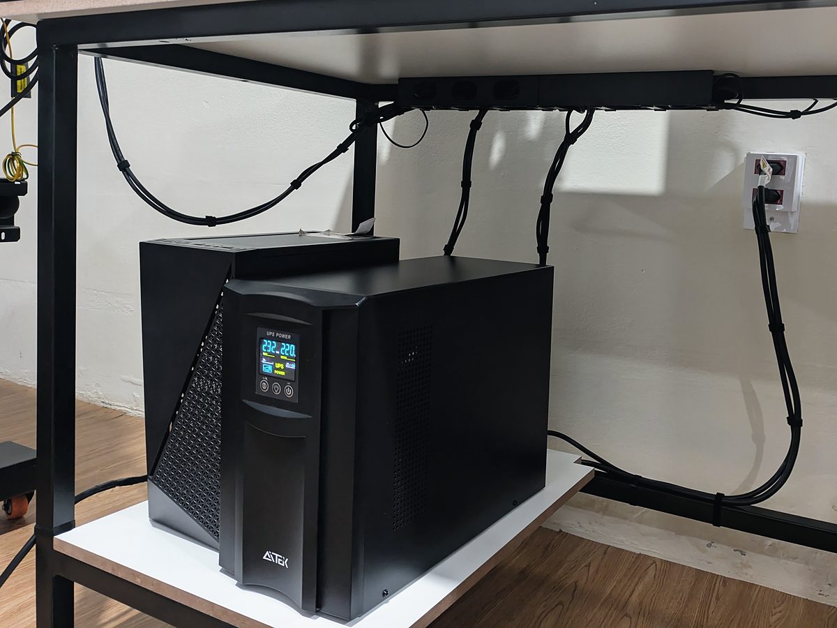 Nobreak sob uma mesa, com cabos de energia presos e organizados