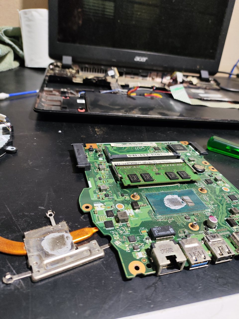 Notebook Acer desmontado sobre a bancada, com a placa-mãe, a memória e o dissipador com pasta térmica à mostra