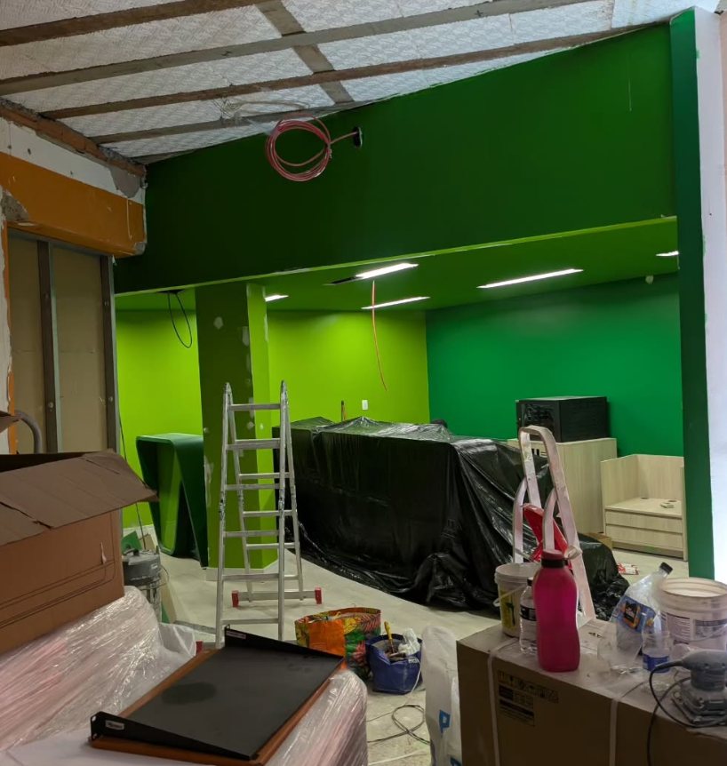 Loja em obra com paredes verdes, teto aberto com cabos passados e escada
