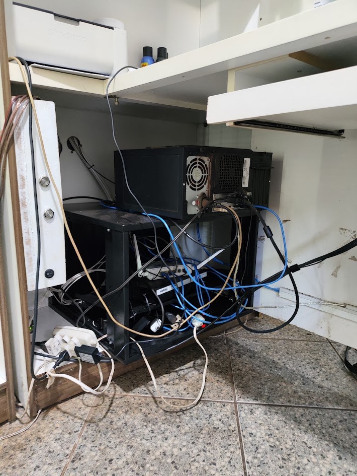 Rack pequeno sob um armário, com cabos soltos e emaranhados, antes da organização