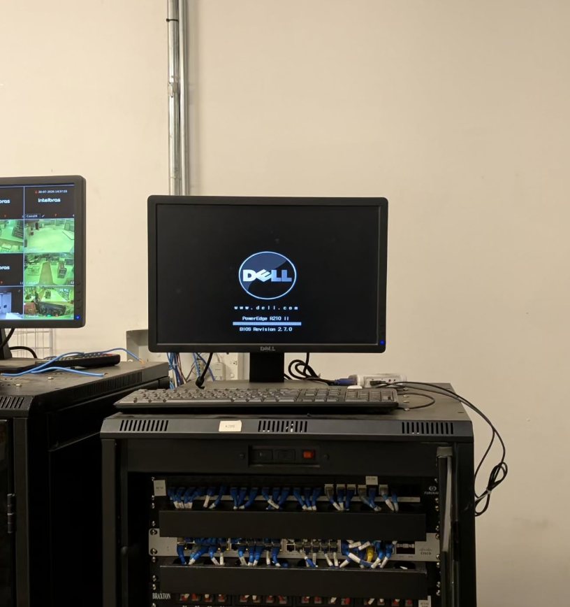 Rack com patch panels e switch, servidor Dell ligado e monitor ao lado mostrando câmeras