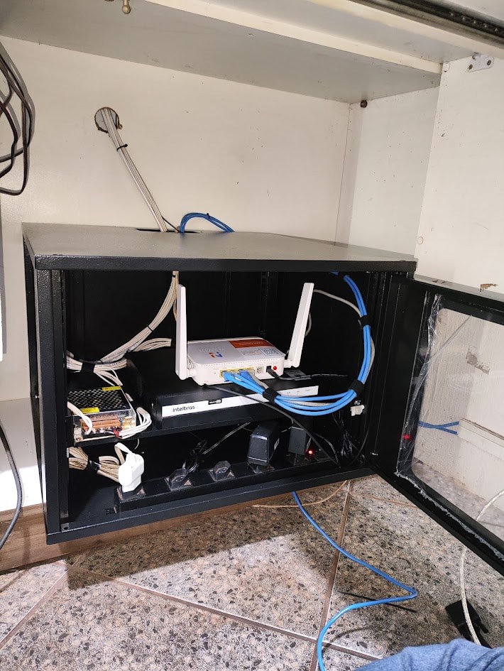 Rack de parede preto com roteador, gravador Intelbras e cabos azuis organizados, depois da organização