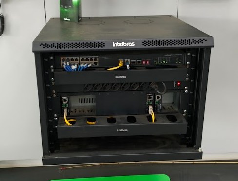 Rack de parede Intelbras com switch, conversores e cabos amarelos organizados