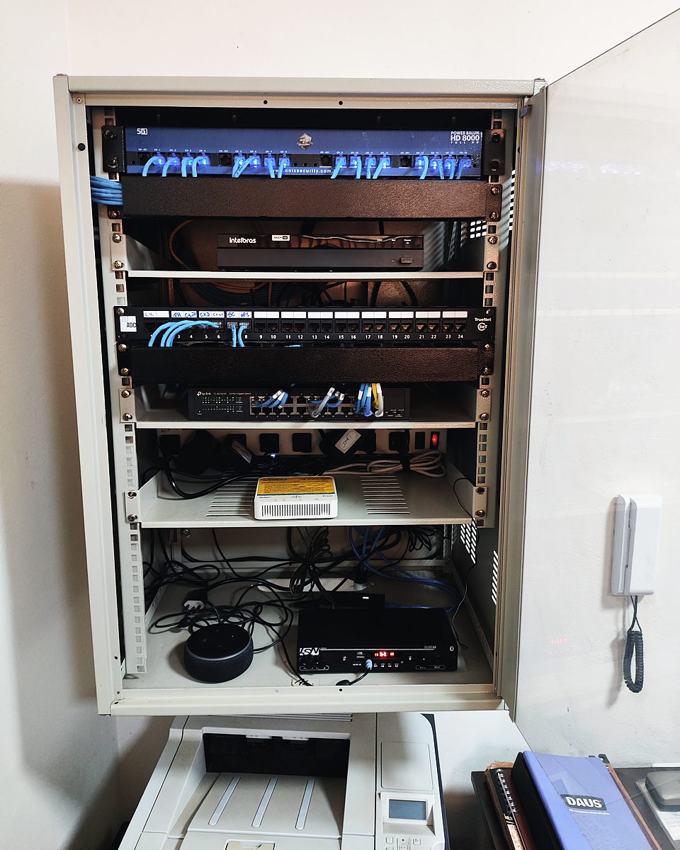 Rack de parede aberto com patch panel, switch e cabos de rede azuis organizados