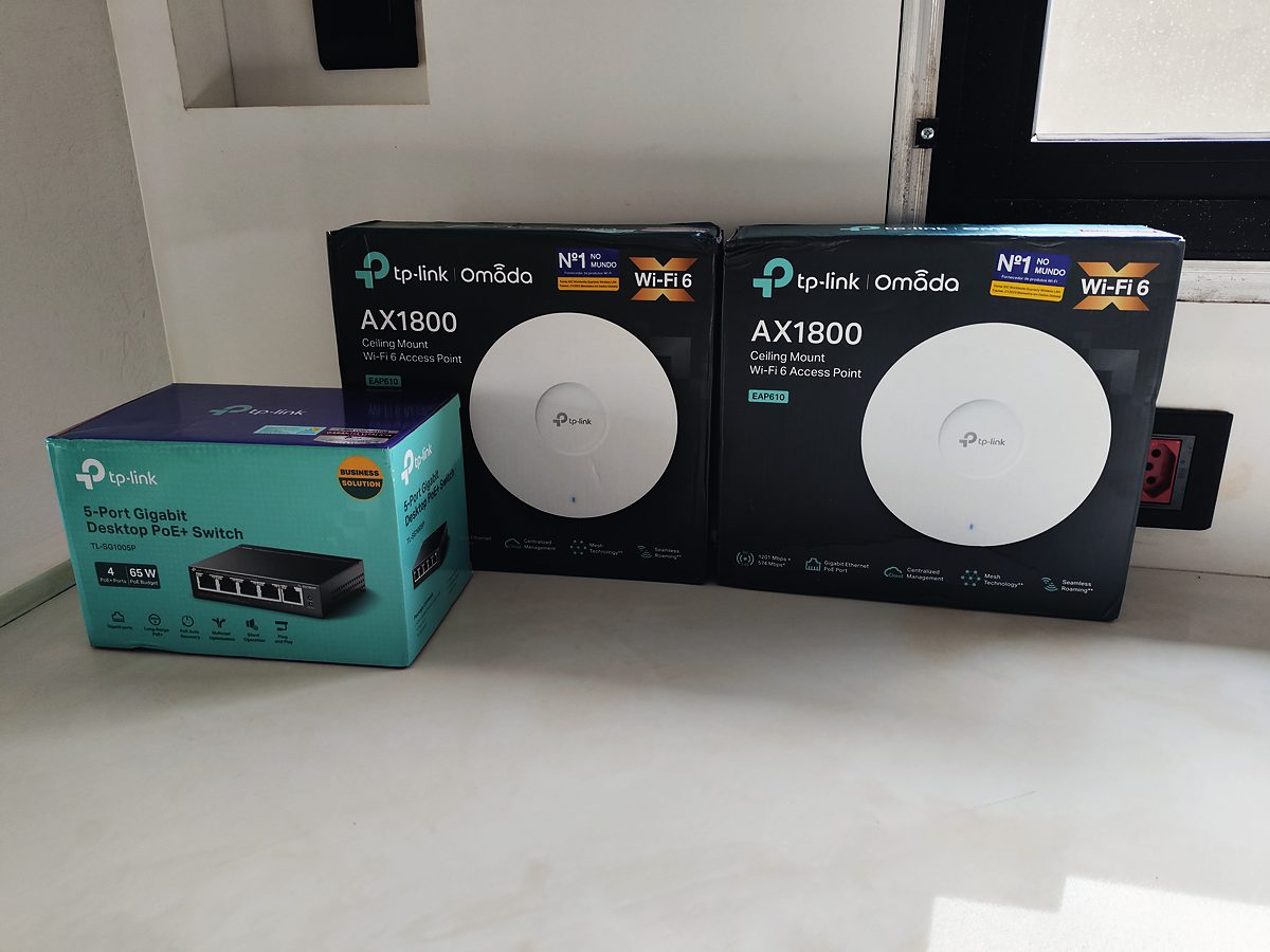 Caixas de pontos de acesso Wi-Fi 6 TP-Link Omada e de um switch PoE sobre uma bancada